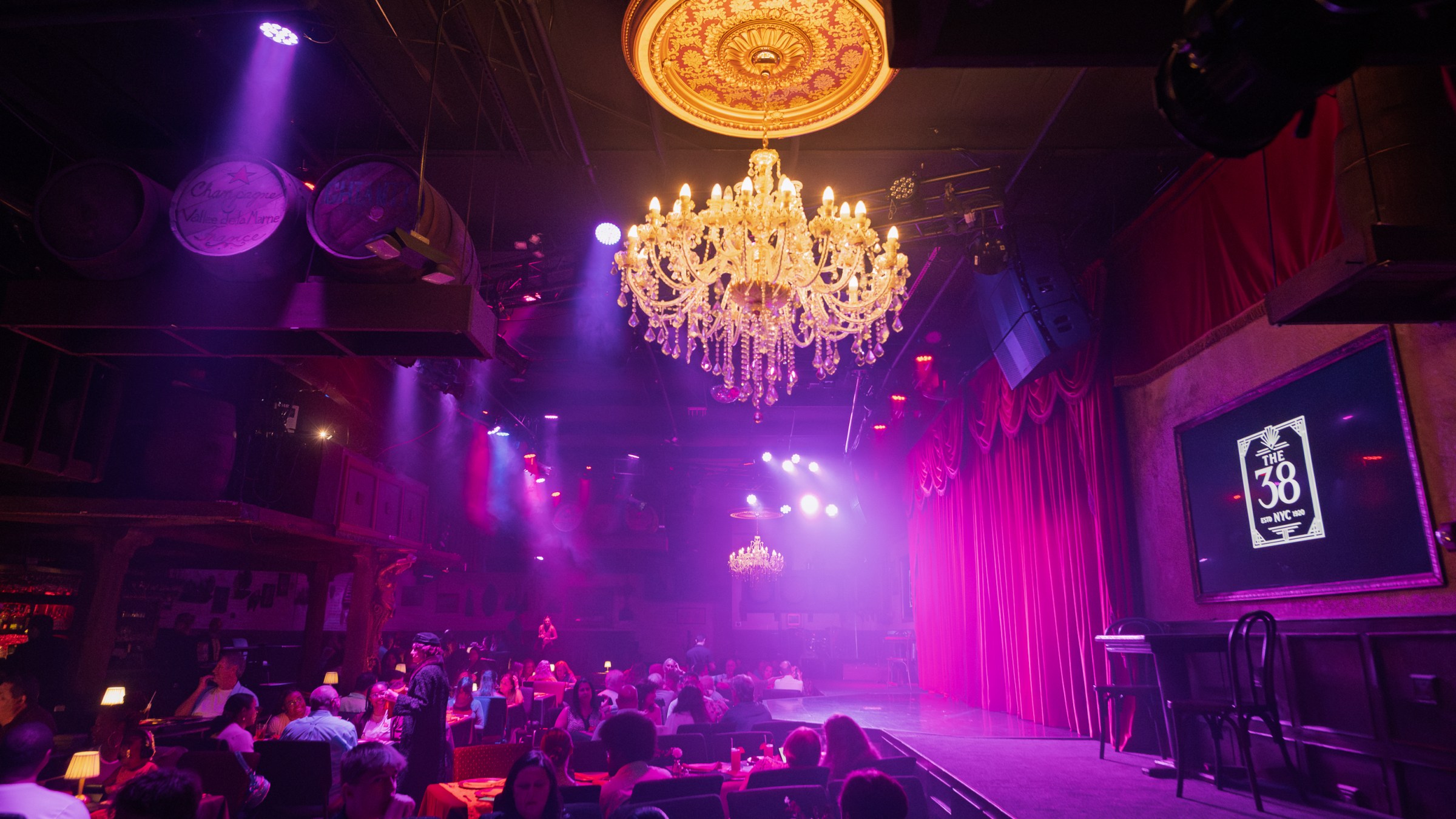 Dimly lit theater with chandeliers, red curtains, and seated audience.