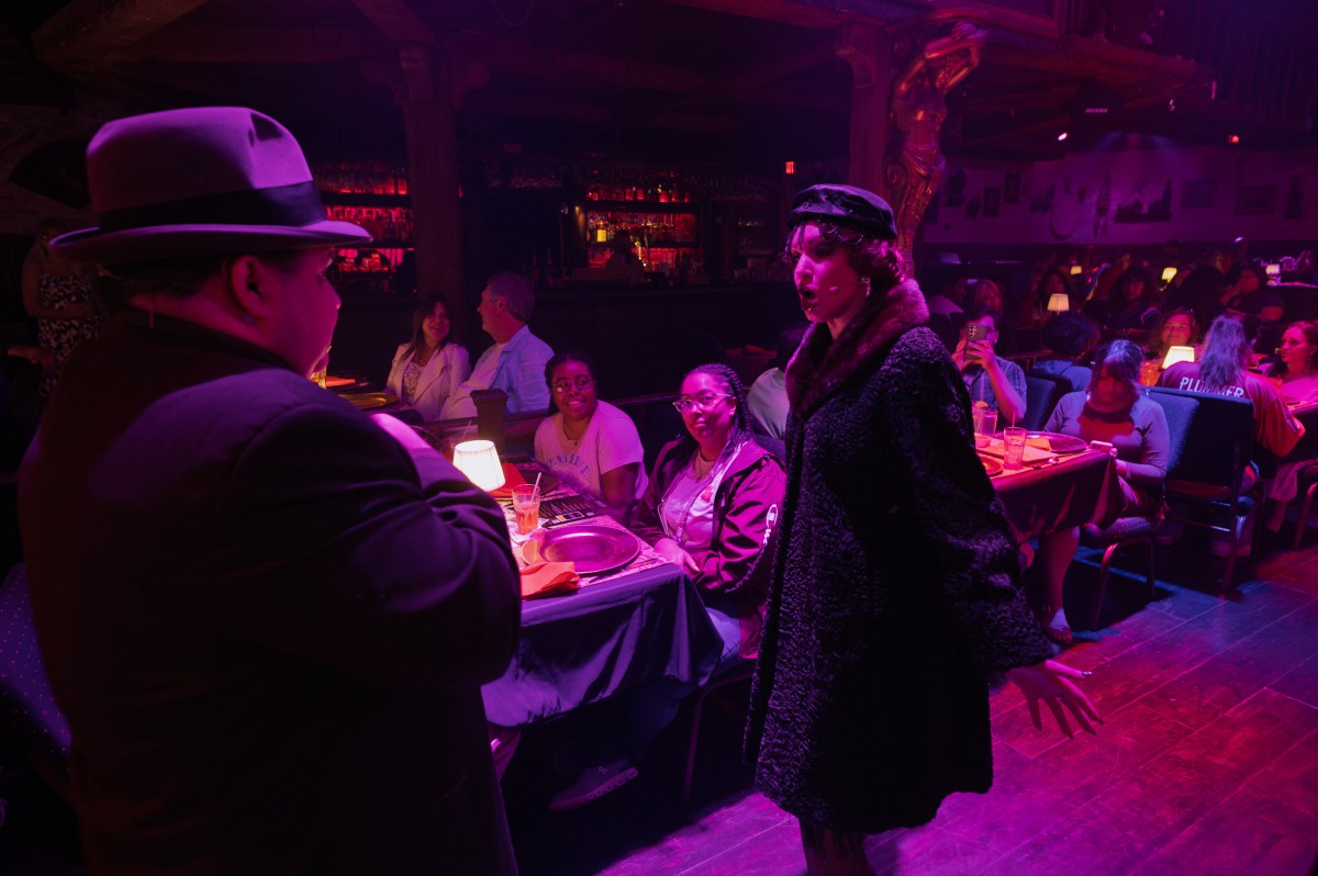 Performers in vintage attire interact with a seated audience in a dimly lit, atmospheric venue.