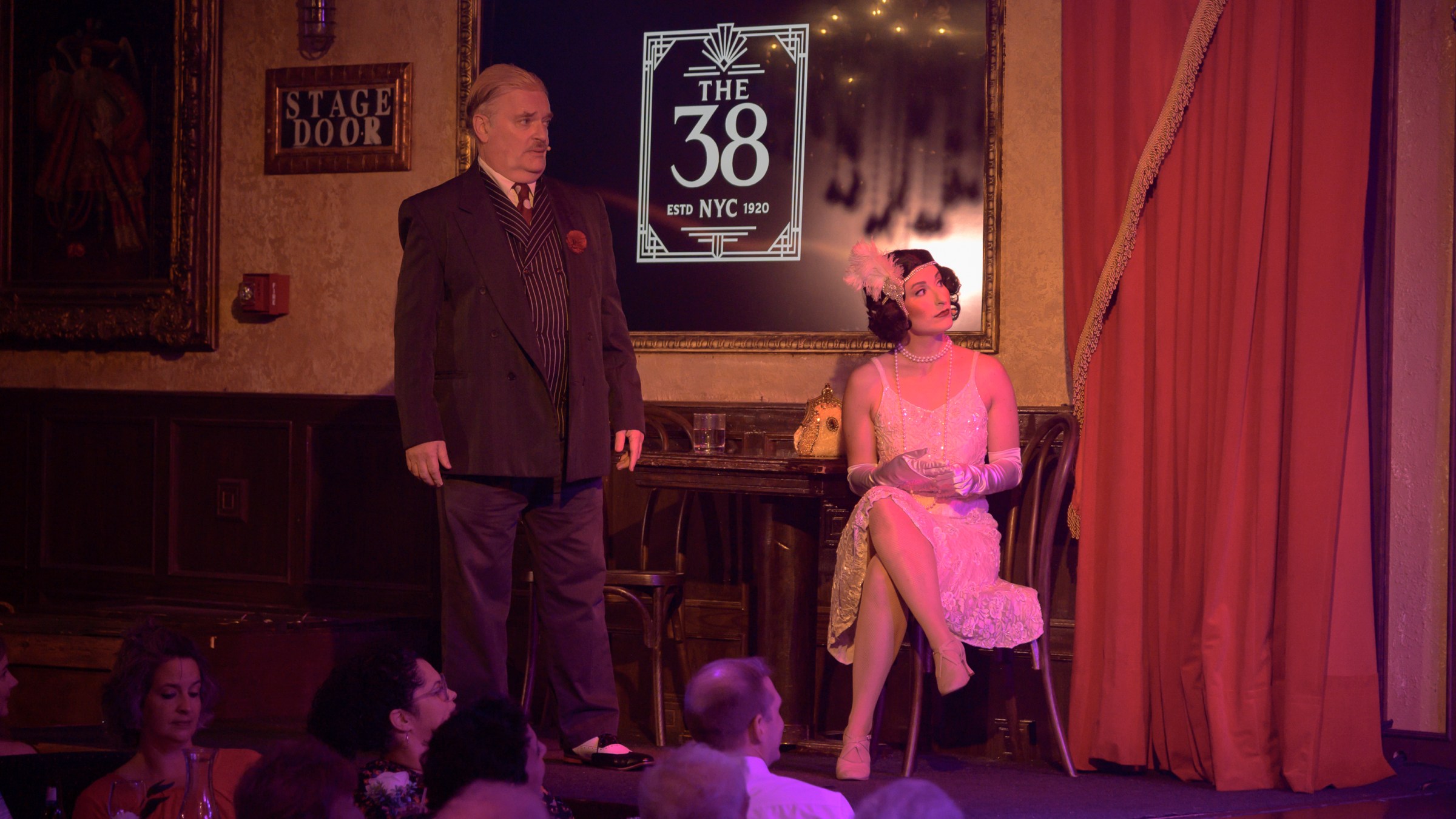 Man and woman in vintage attire on stage with 'The 38' sign behind them.