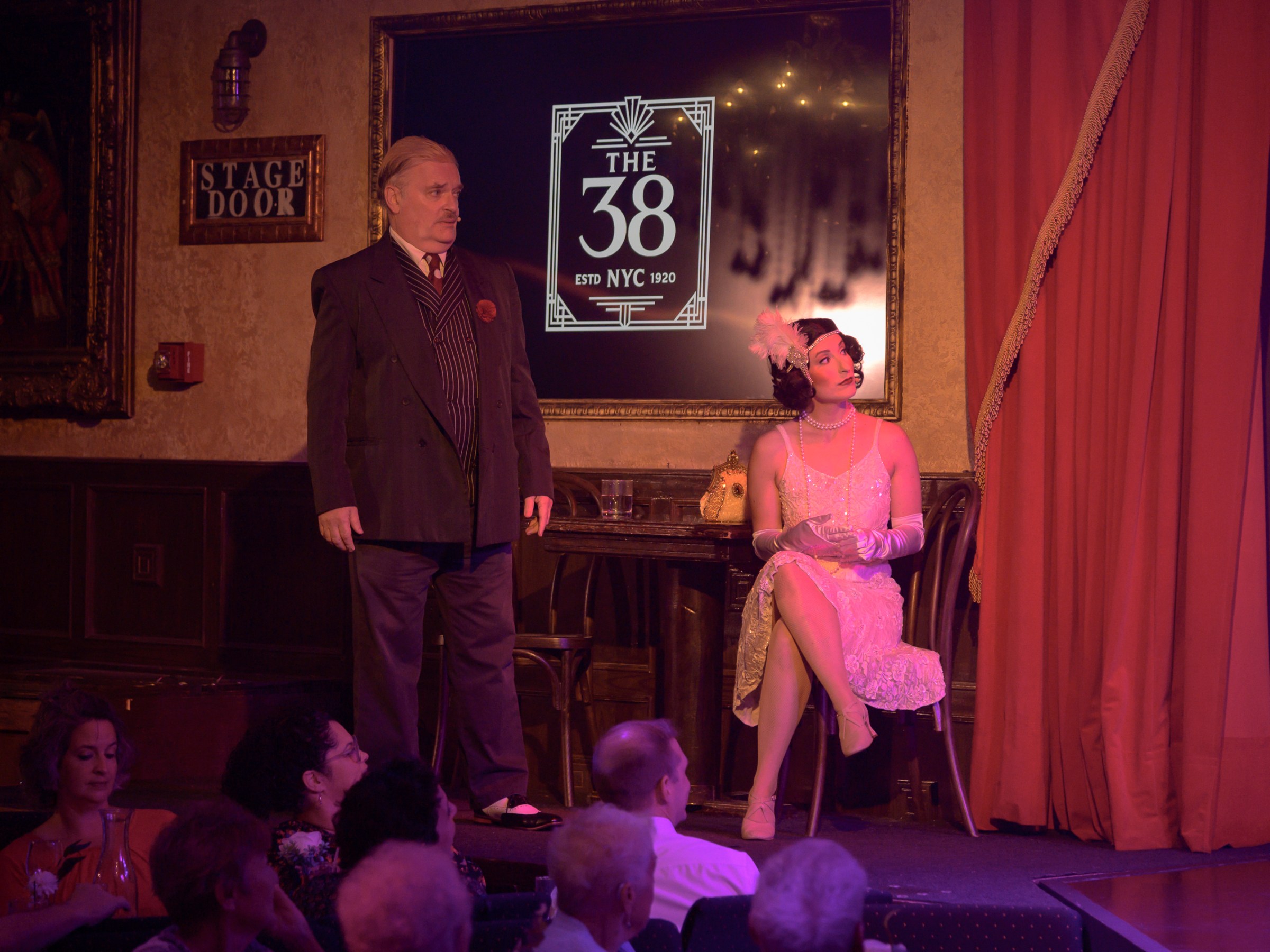 Man and woman in vintage attire on stage with 'The 38' sign behind them.