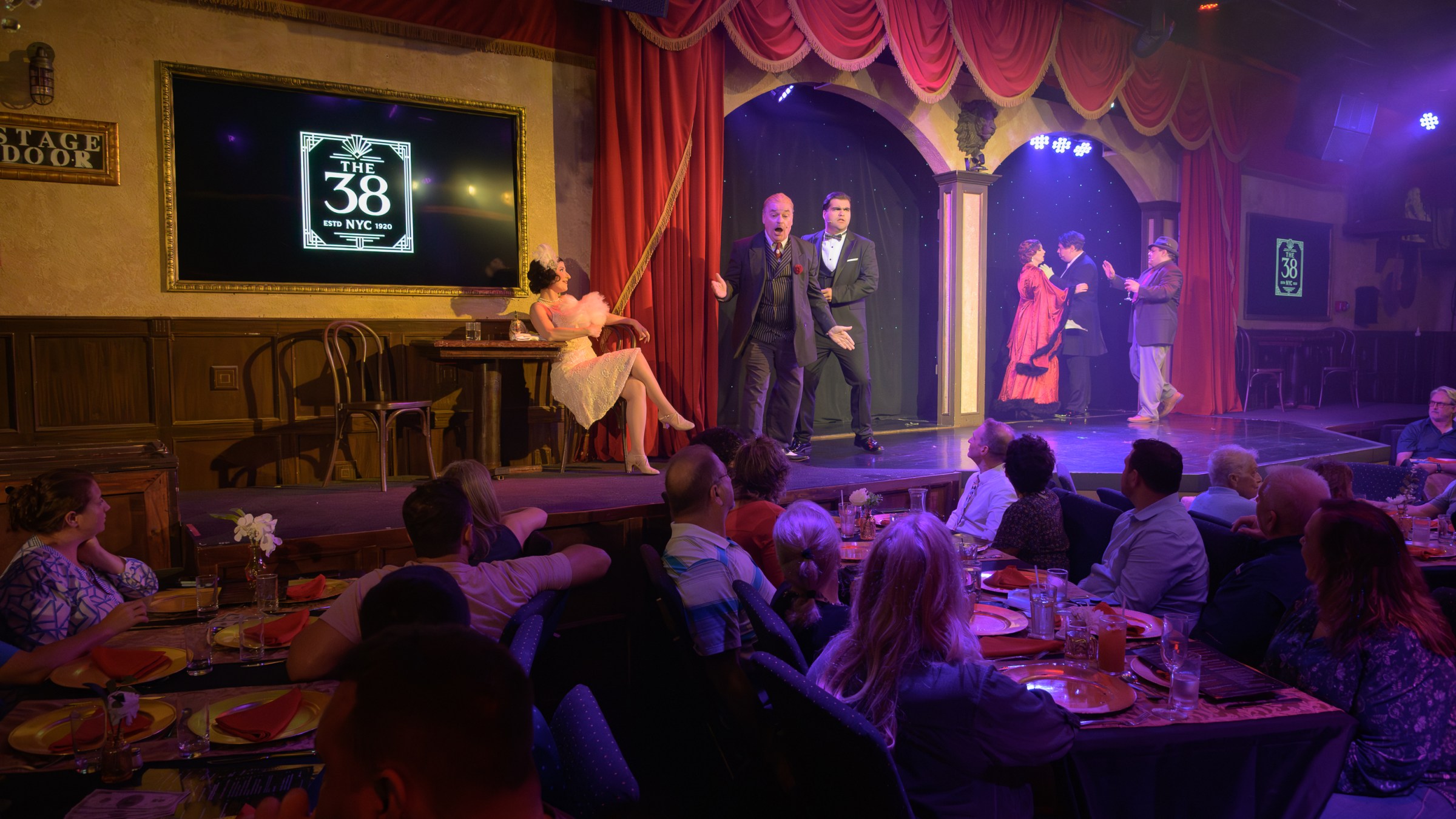 Dinner theater performance with actors on stage and audience seated at tables.