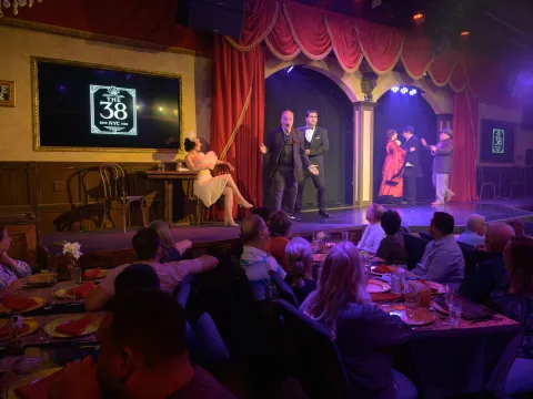 Dinner theater performance with actors on stage and audience seated at tables.