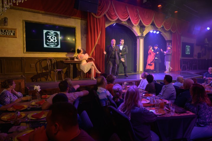 Dinner theater performance with actors on stage and audience seated at tables.