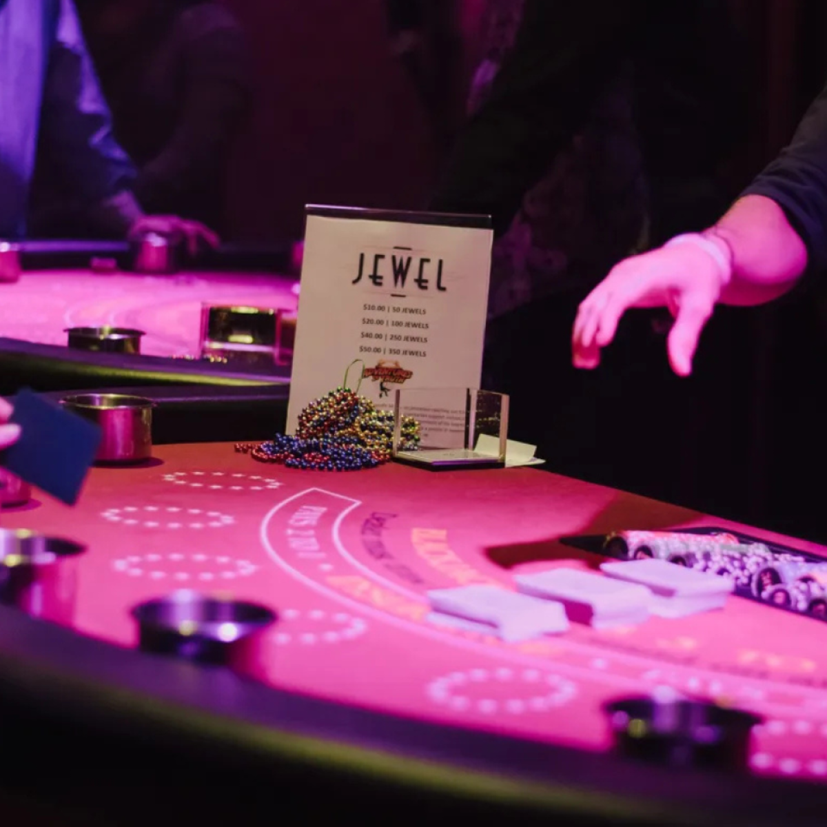 People at a casino table with chips and a sign reading 'Jewel'.