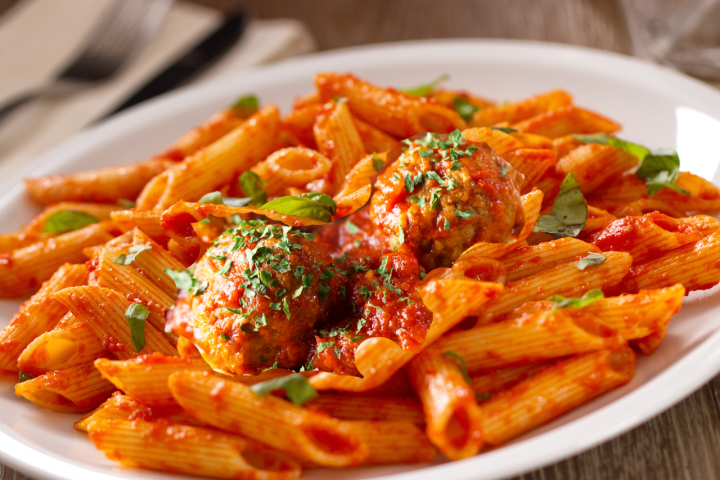 Plate of penne pasta with tomato sauce, meatballs, and basil garnish.