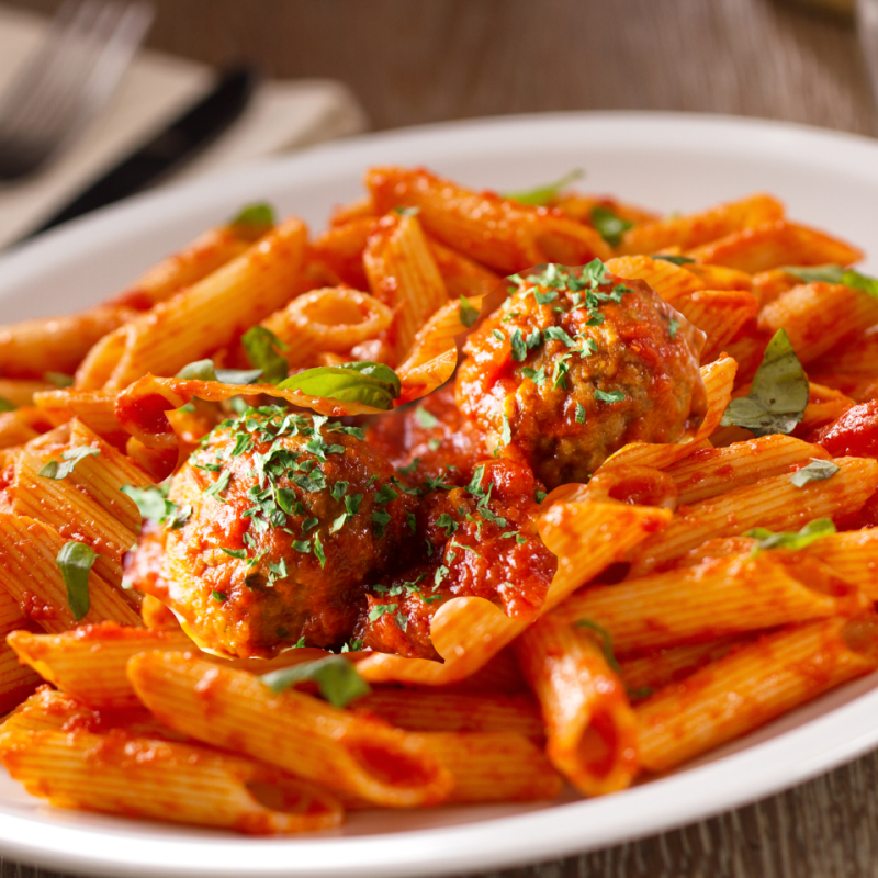 Plate of penne pasta with tomato sauce, meatballs, and basil garnish.