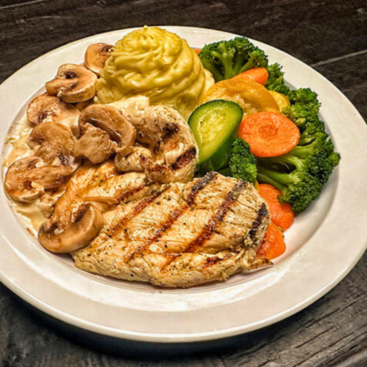 Grilled chicken with mushrooms, mashed potatoes, and mixed vegetables on a plate.