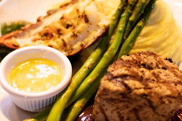 Grilled steak, lobster tail, asparagus, mashed potatoes, and sauce on a plate.