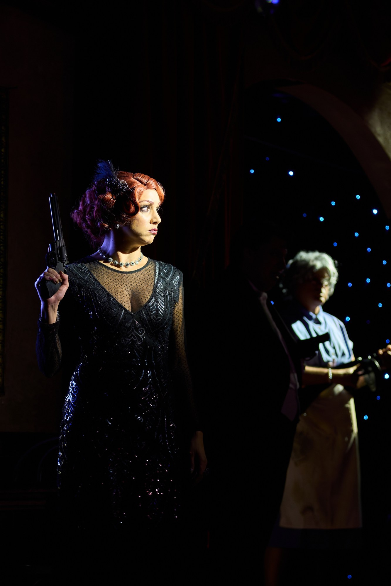 Woman in black dress with red hair holding a gun on stage.