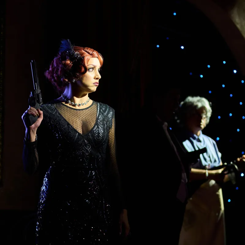 Woman in black dress with red hair holding a gun on stage.