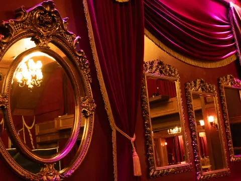Luxurious room with ornate mirrors, red drapes, and chandelier lighting.