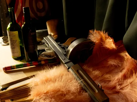 Shotgun, bottles, and pink feathers on a table.
