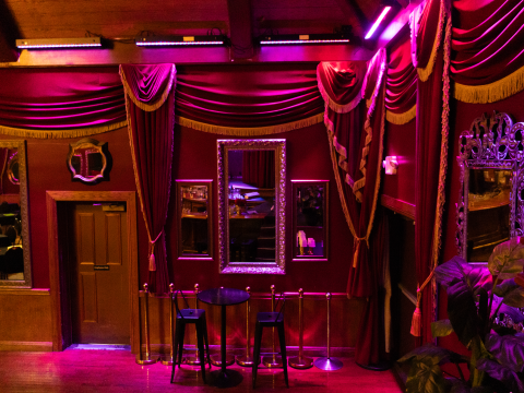 Elegant room with purple lighting, ornate curtains, mirrors, and a small table with stools.