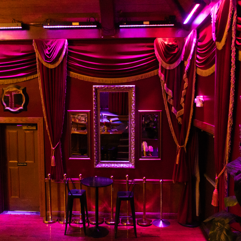 Elegant room with purple lighting, ornate curtains, mirrors, and a small table with stools.