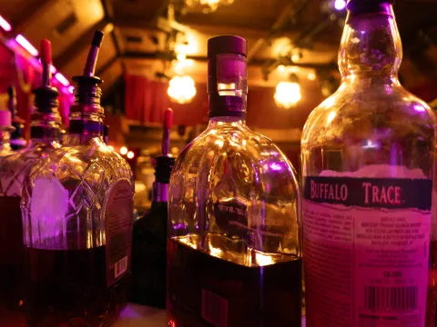 Close-up of assorted liquor bottles on a bar with purple ambient lighting.