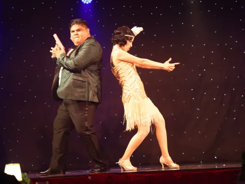 Two people in 1920s costumes perform a playful dance on stage.