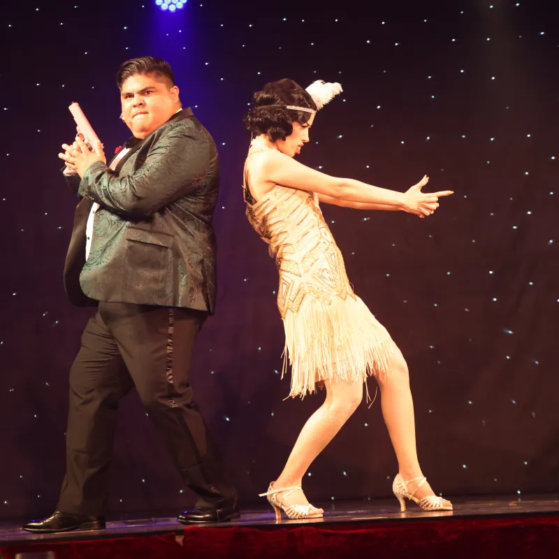 Two people in 1920s costumes perform a playful dance on stage.