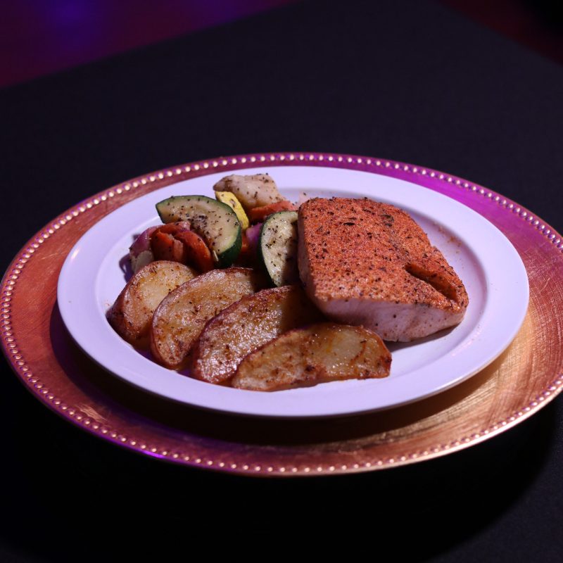 Plate with seasoned fish, roasted vegetables, and potato wedges on a gold charger.