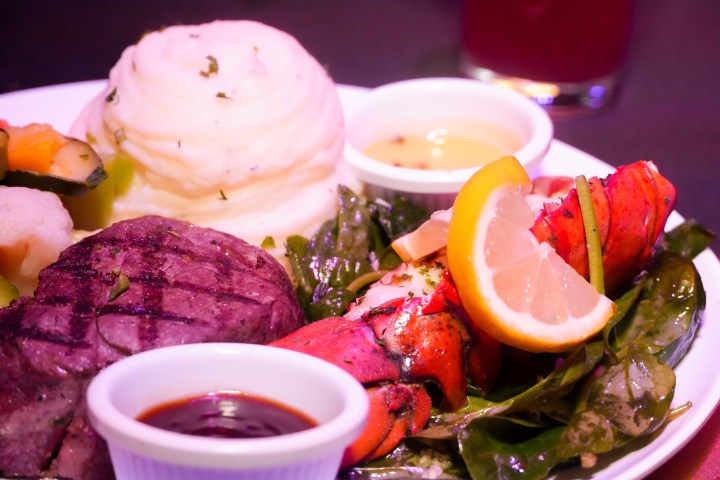 Plate with steak, lobster tail, mashed potatoes, sauce cups, and lemon slices.